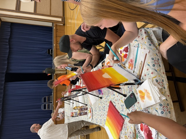 A long table of painters working at their easels in the cultural hall