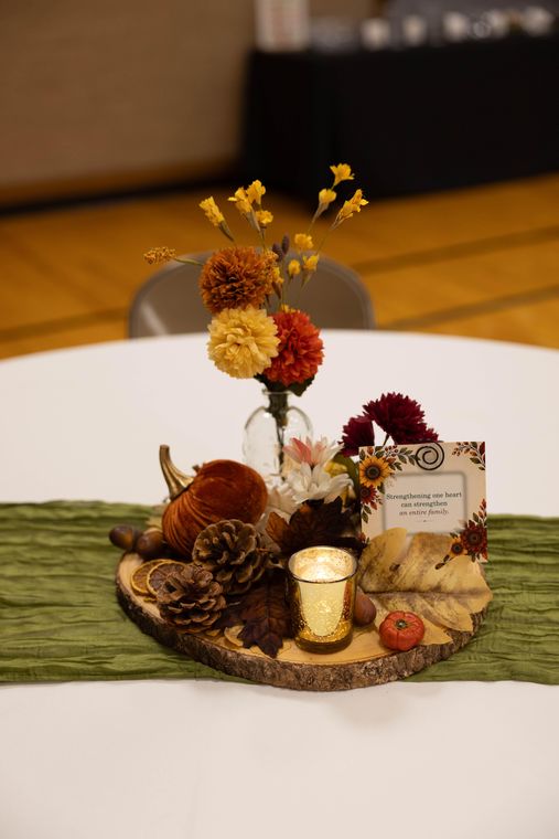 A fall centerpiece of flowers, pinecones, pumpkins, and a candle on a wood round